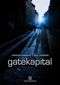 Sosiologi-bok om gatekapital av Universitetsforlaget, vises foran en bokhylle med andre akademiske bøker.